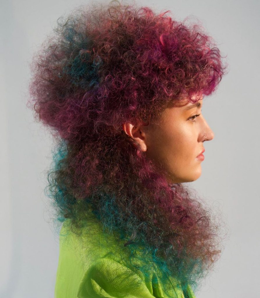 A woman with a modern curly mullet, dyed in fuschia and blue by stylist Andy Judd